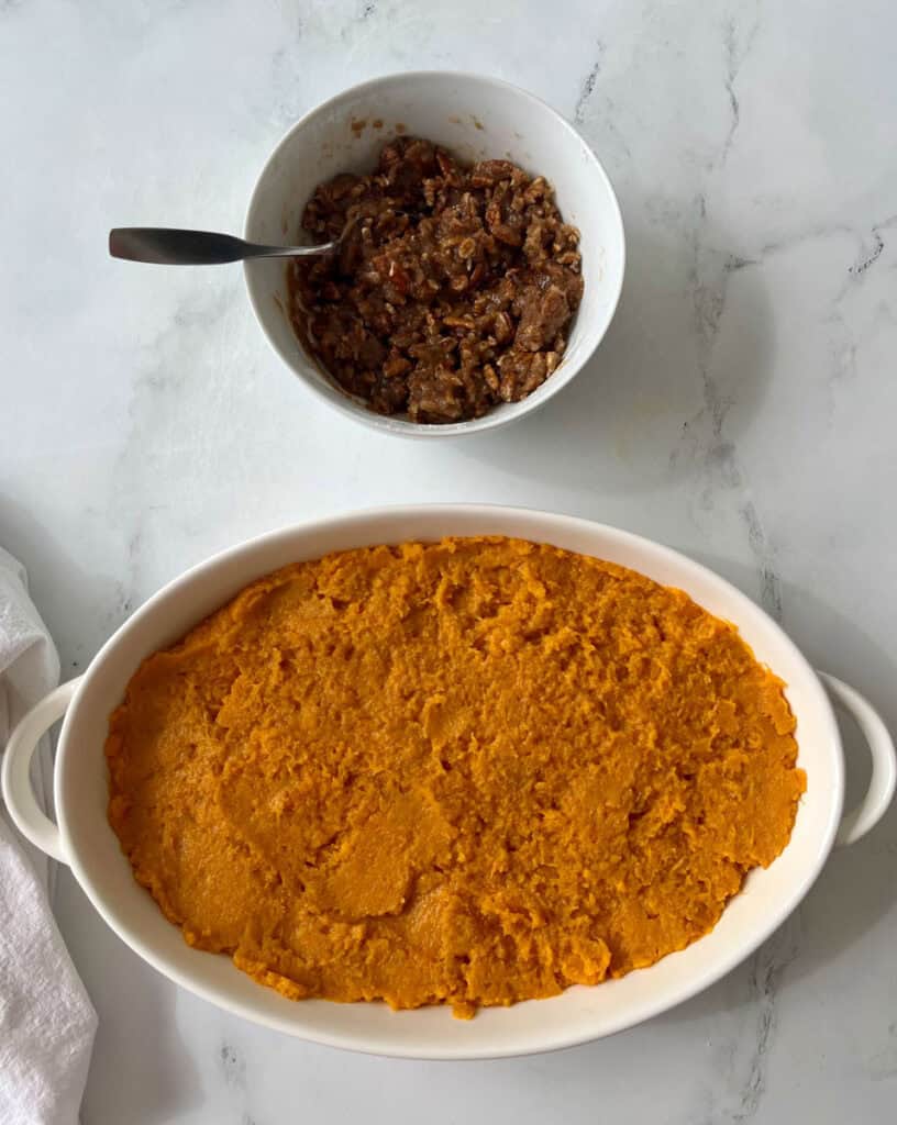 Sweet potato casserole in a white dish with a bowl of pecan topping.