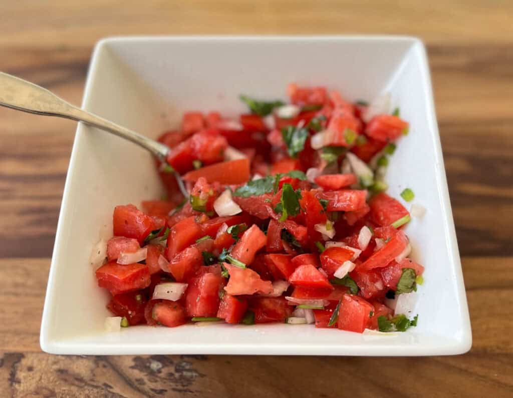A white bowl filled with chopped tomatoes and herbs.