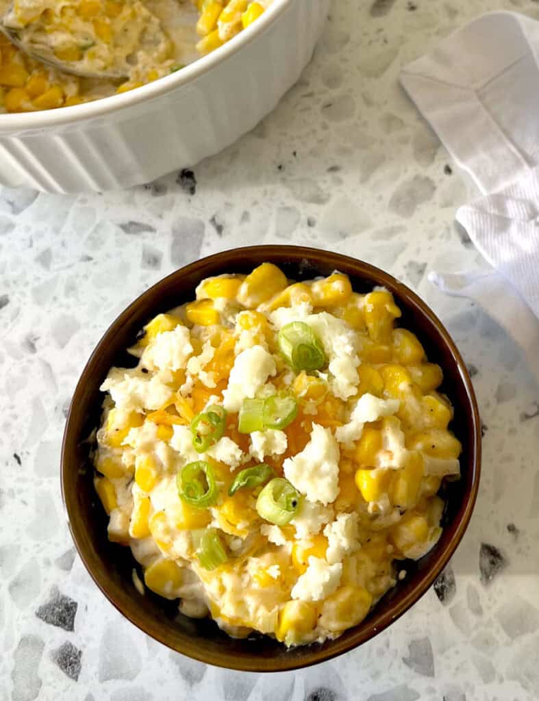 A bowl of corn and cheese with a spoon.