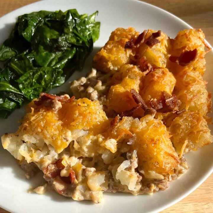 Tater Tot Casserole with Crispy Bacon Bits on a plate with sautéed spinach.