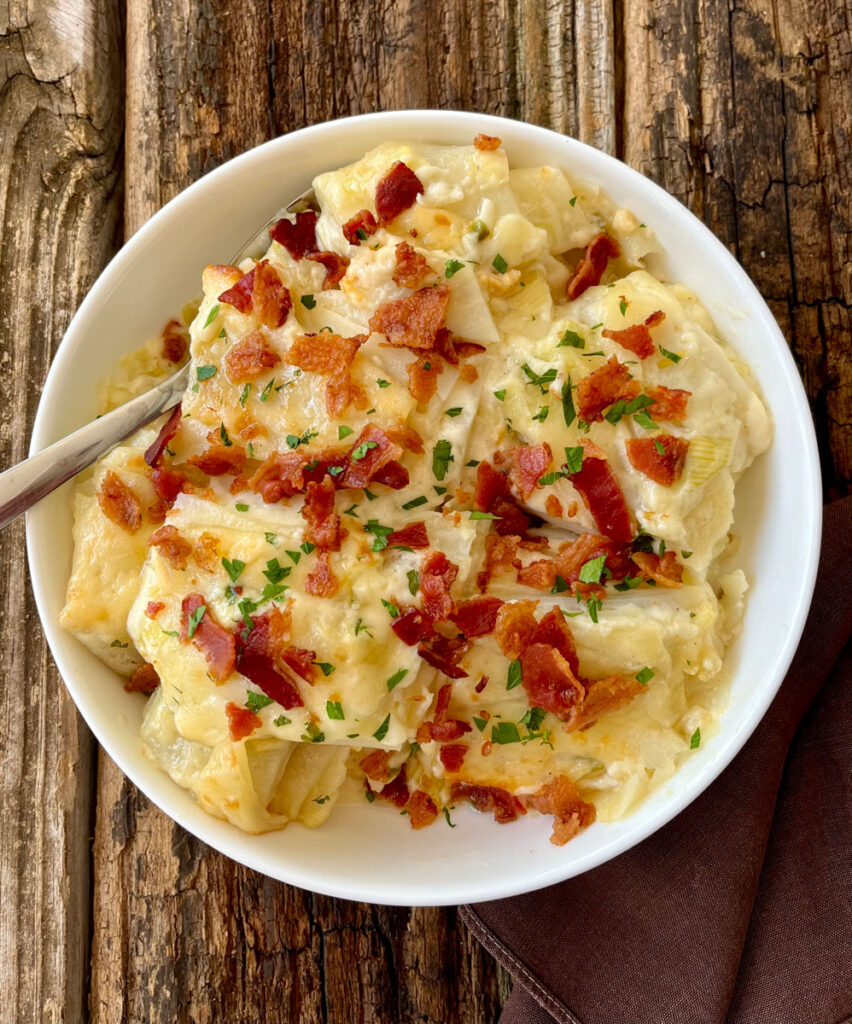 Cheese potato casserole with crumbled bacon on top in a white bowl.