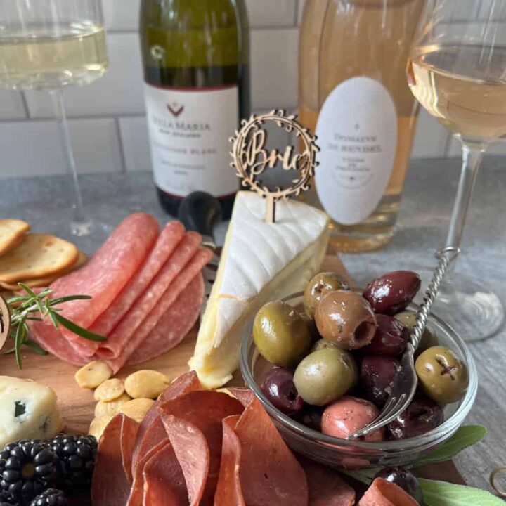 Variety of meat, cheese, fruit, and condiments with bottles of wine.