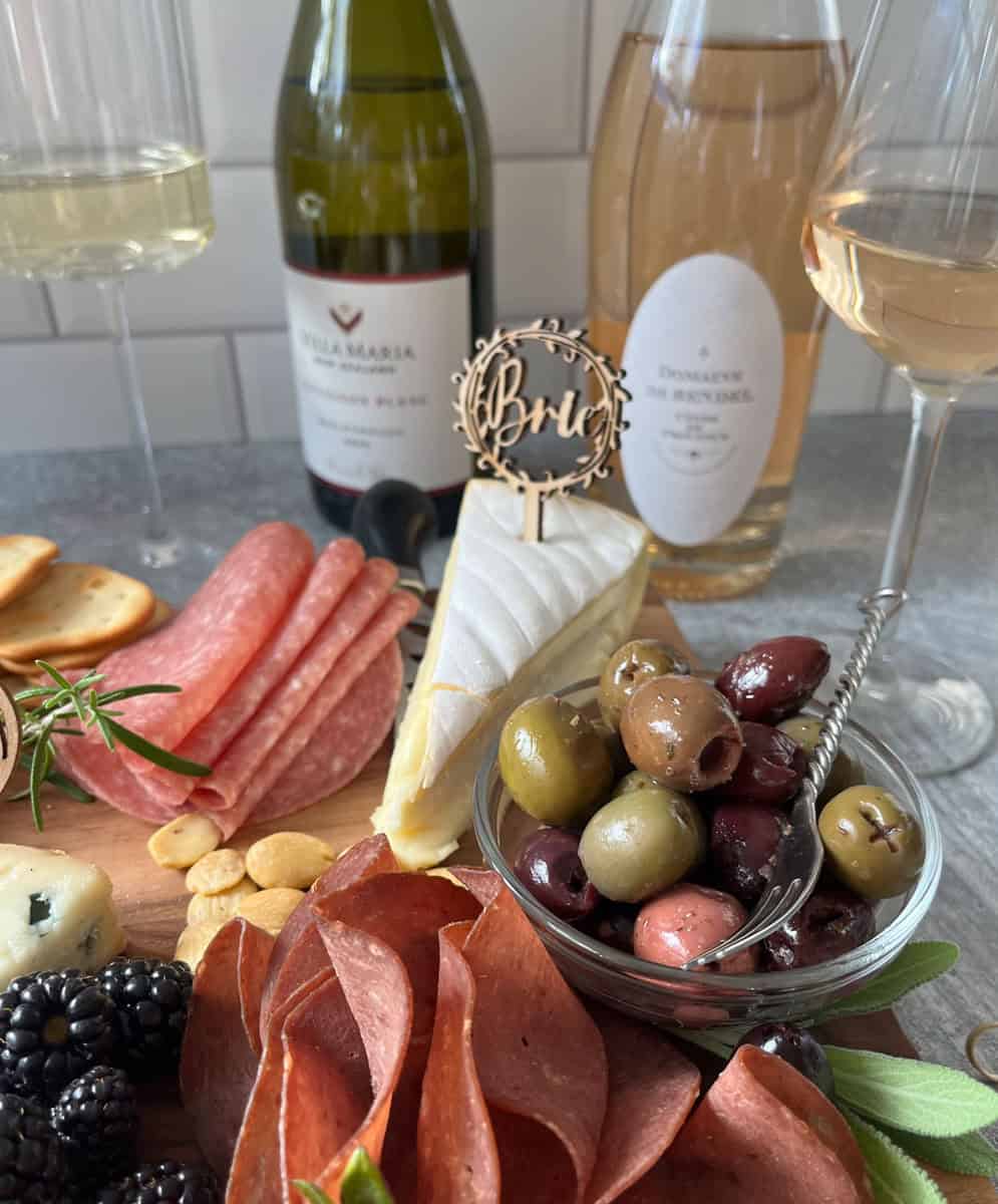 Variety of meat, cheese, fruit, and condiments with bottles of wine.