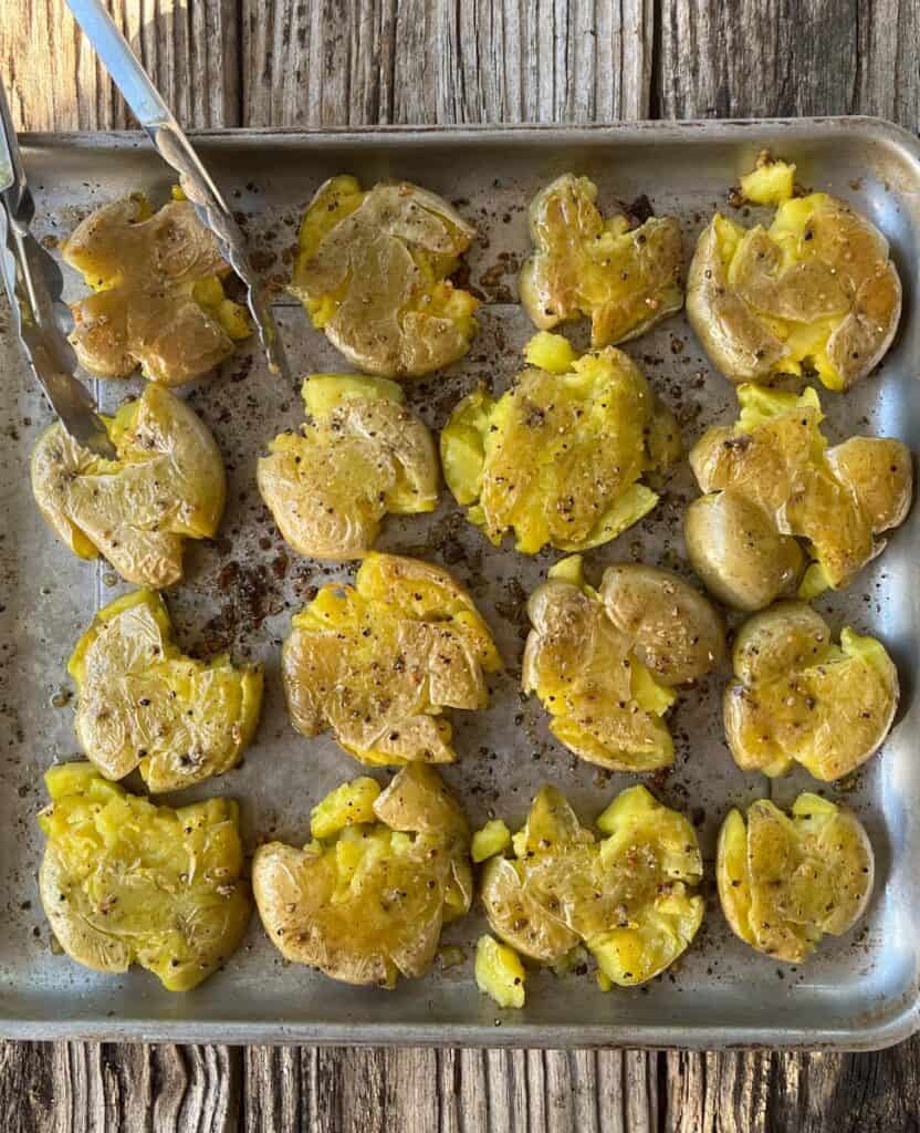 Roasted smashed potatoes on a baking sheet with tongs.