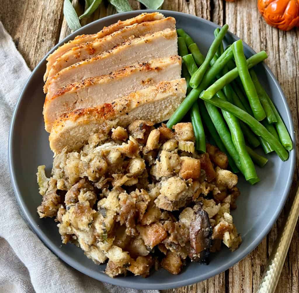 Sliced chicken breast with green beans and stuffing on a gray plate.