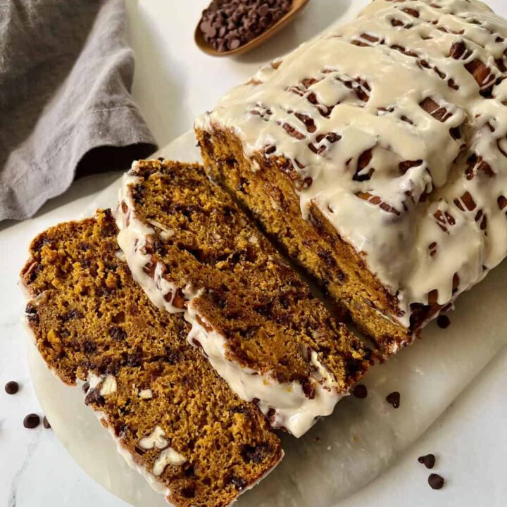 Sliced glazed pumpkin bread with chocolate chips and pecans on a marble board.
