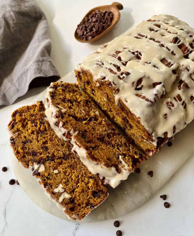 Sliced glazed pumpkin bread with chocolate chips and pecans on a marble board.