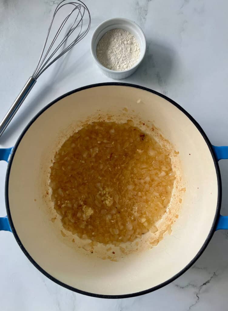 Chopped onion and garlic cooking in a blue Dutch oven on a white surface.
