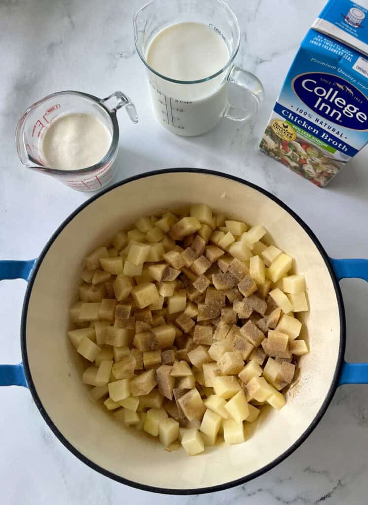 Diced potatoes in a large pot with milk and chicken broth, with ingredients for homemade potato soup.