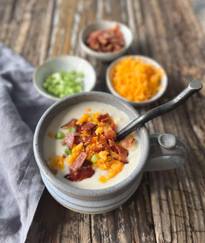 Creamy potato soup topped with bacon, cheese, and green onions on rustic wooden table.