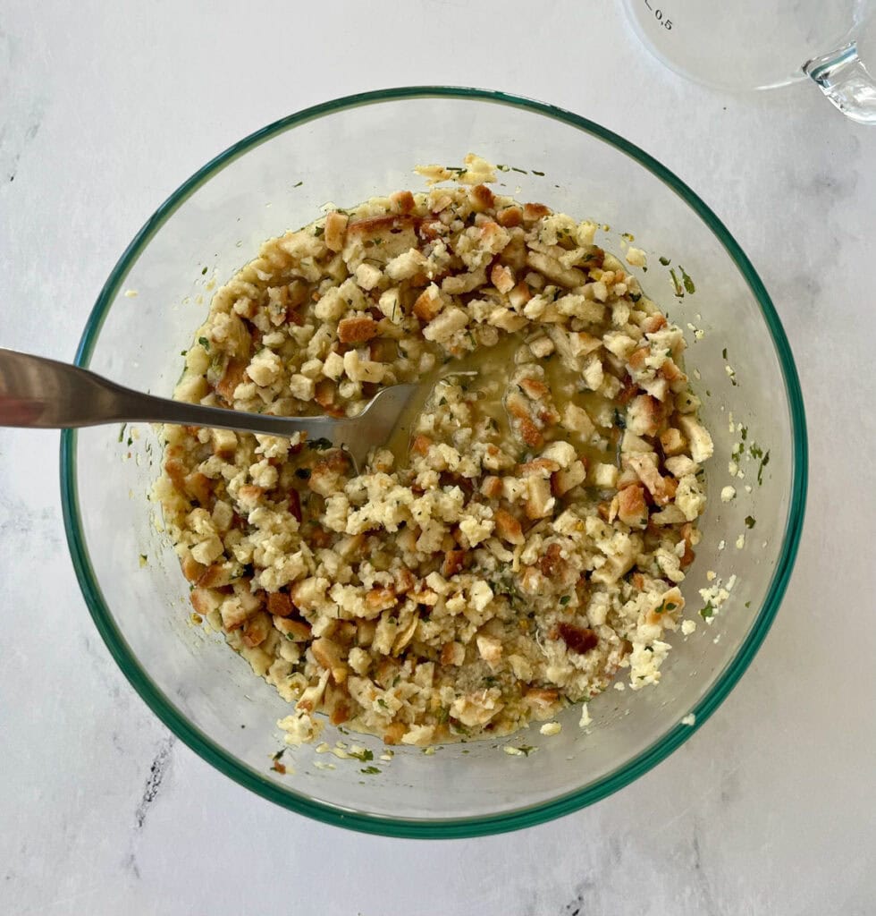 Stuffing mixture in glass bowl with a fork on a white marble surface.