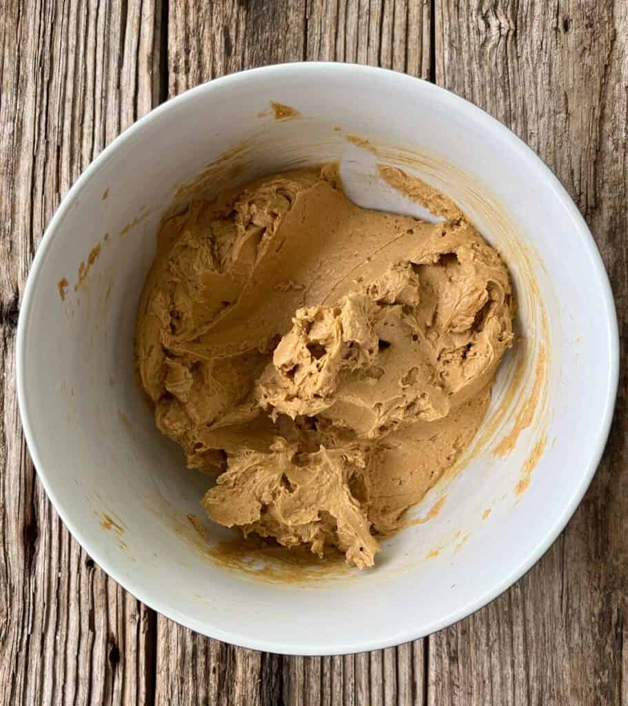 Large mixing bowl with cookie dough in it on a wooden surface.