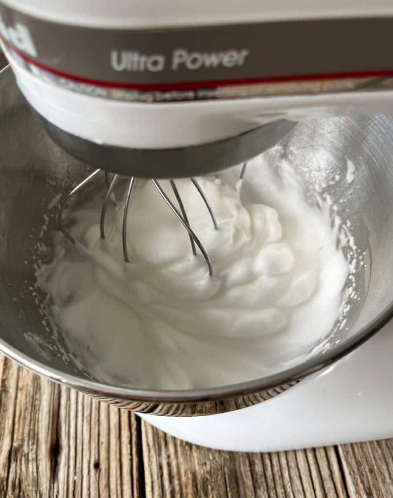 Marshmallow filling in mixing bowl with stand mixer, close-up, on wooden surface.