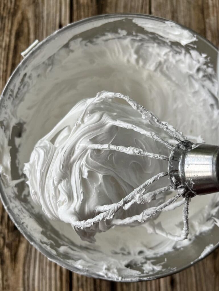 Creamy marshmallow filling in a metal mixing bowl with beaters attached.