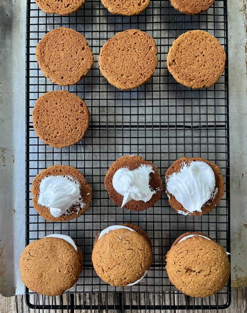 Soft baked cookies cooling on a wire rack, some with marshmallow filling on them.