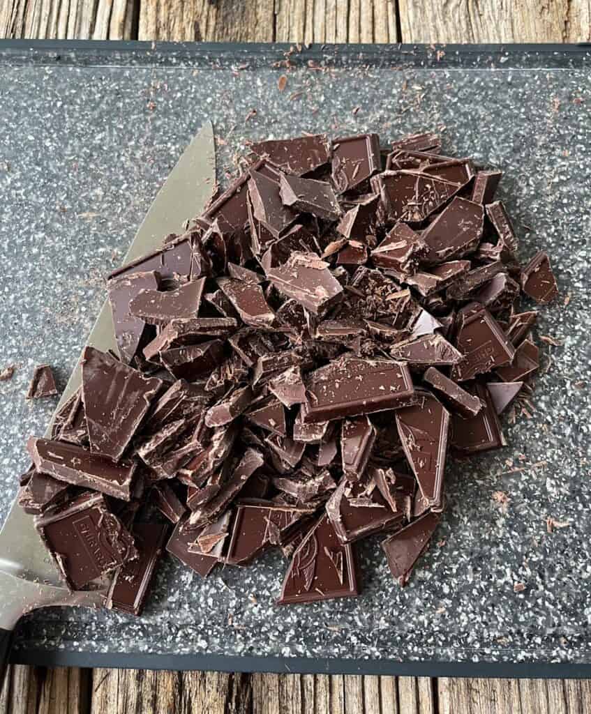 Rich dark chocolate broken into pieces on a cutting board.