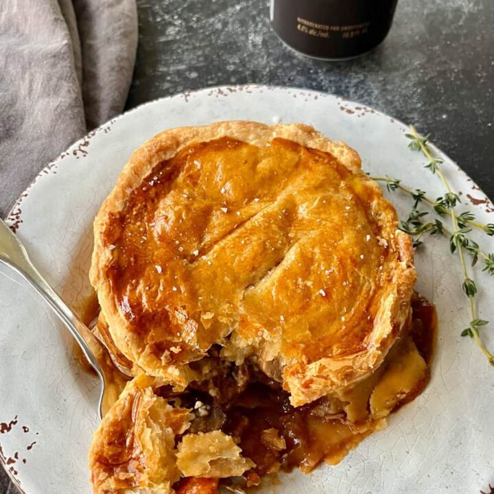 Beef pie with flaky crust served on a rustic white plate.