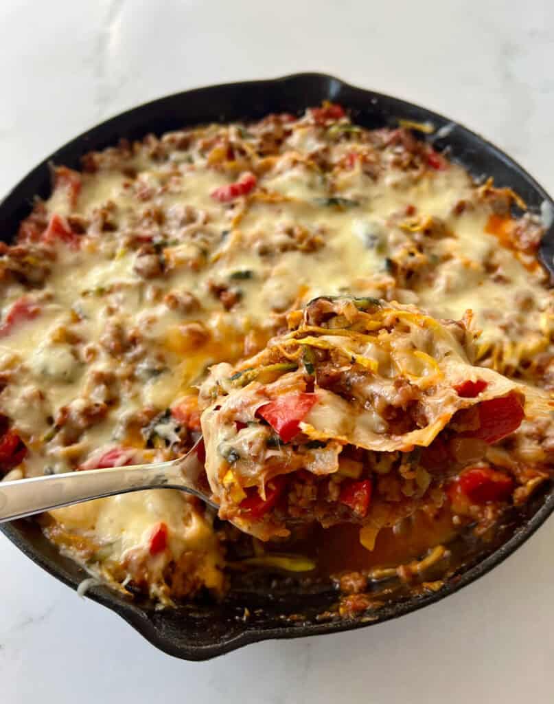 Zucchini and sausage casserole in a cast iron skillet with melted cheese on top.