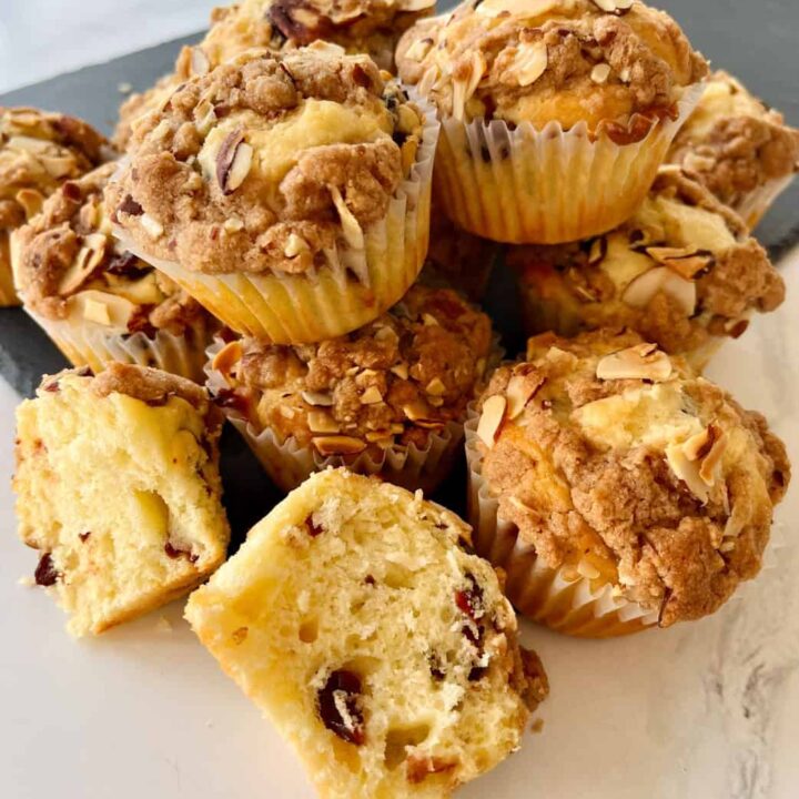 Dried cherry muffins with an almond crumb topping on a marbled surface.
