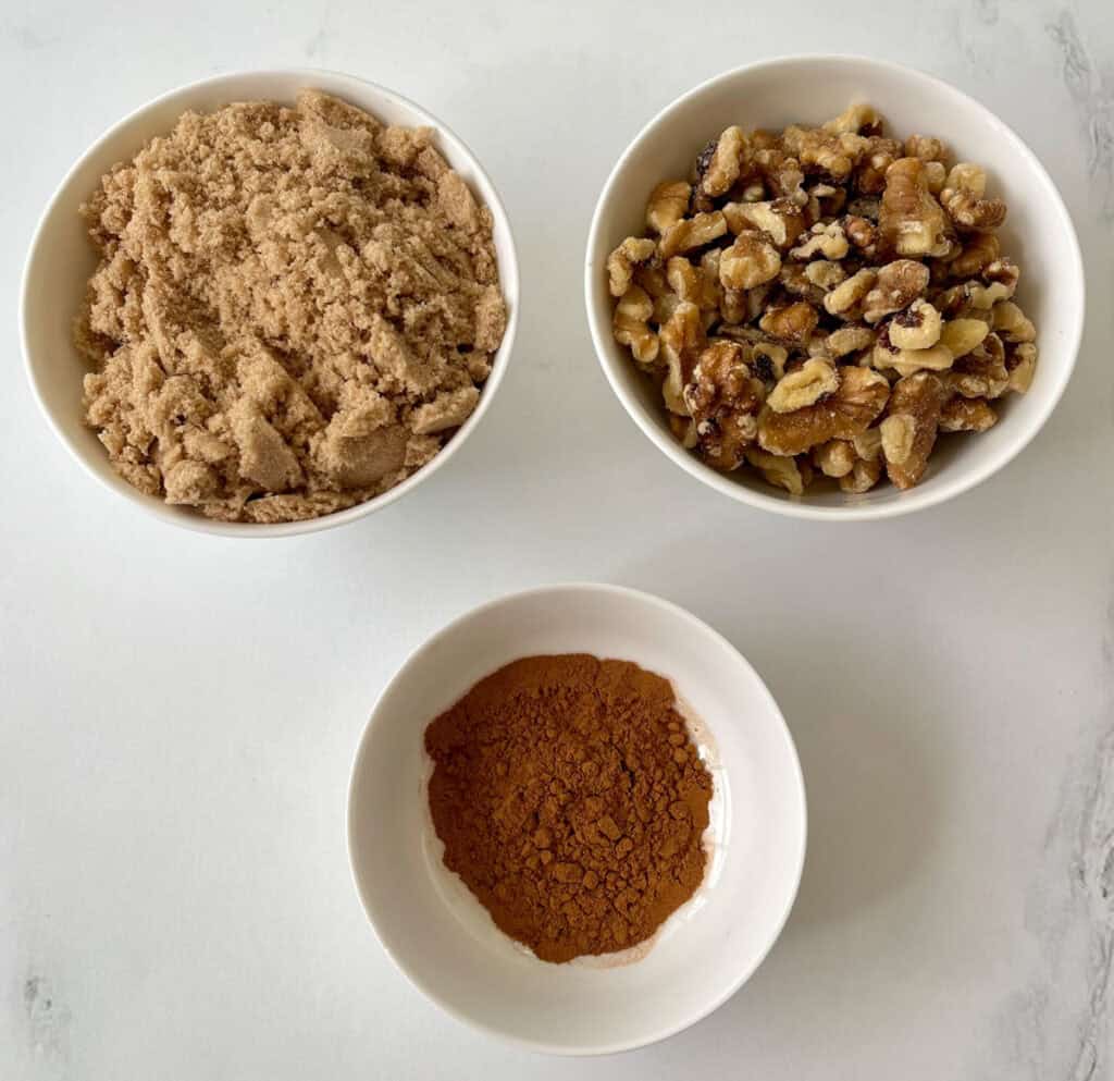 Assorted baking ingredients: brown sugar, chopped walnuts, and ground cinnamon in small bowls for streusel topping.