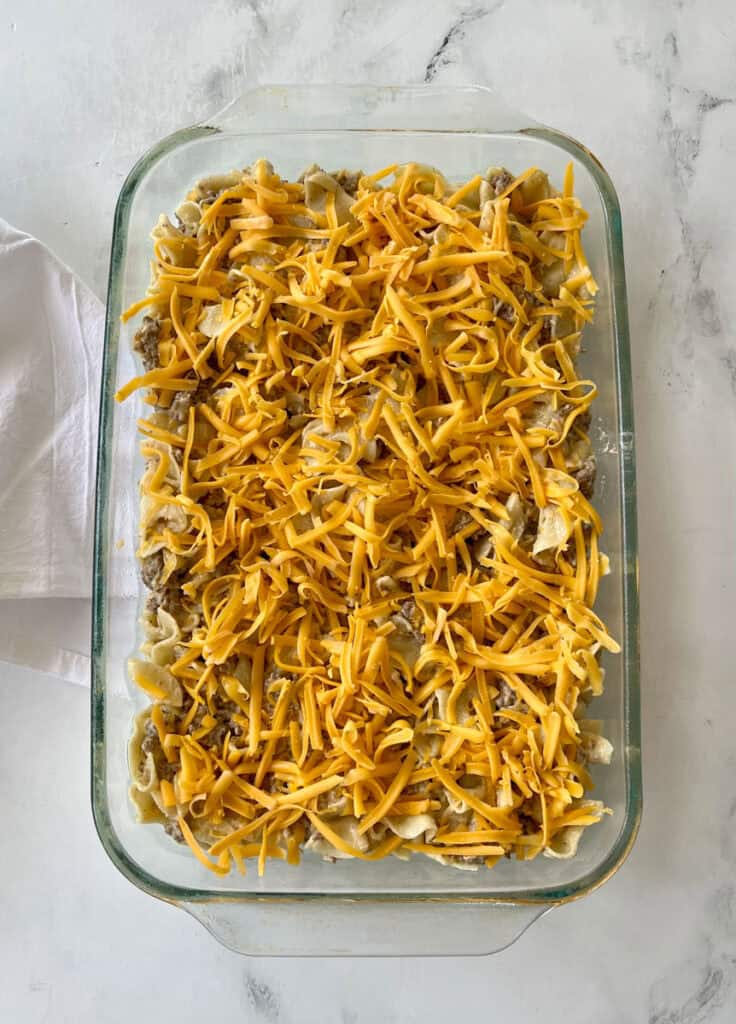 Cheesy beef and noodle casserole in a glass baking dish, ready for baking.