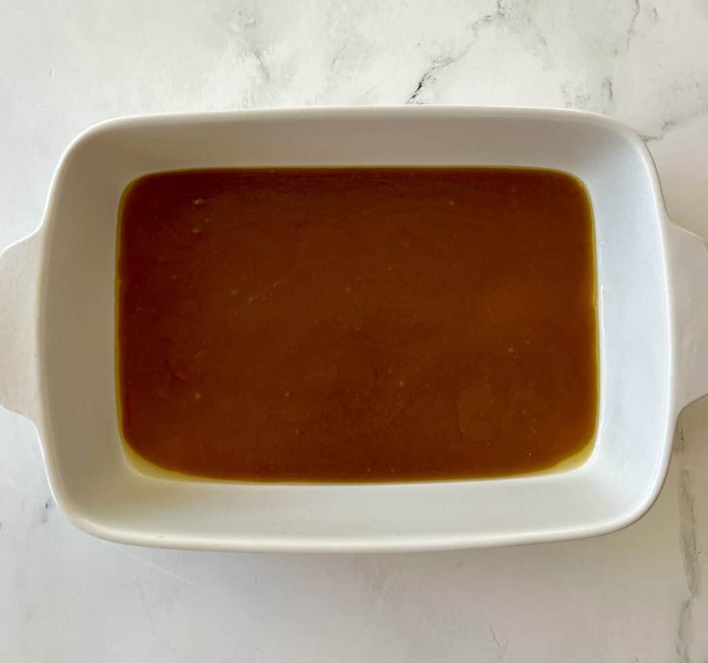 Melted butter with brown sugar mixture on the bottom of a white baking dish.