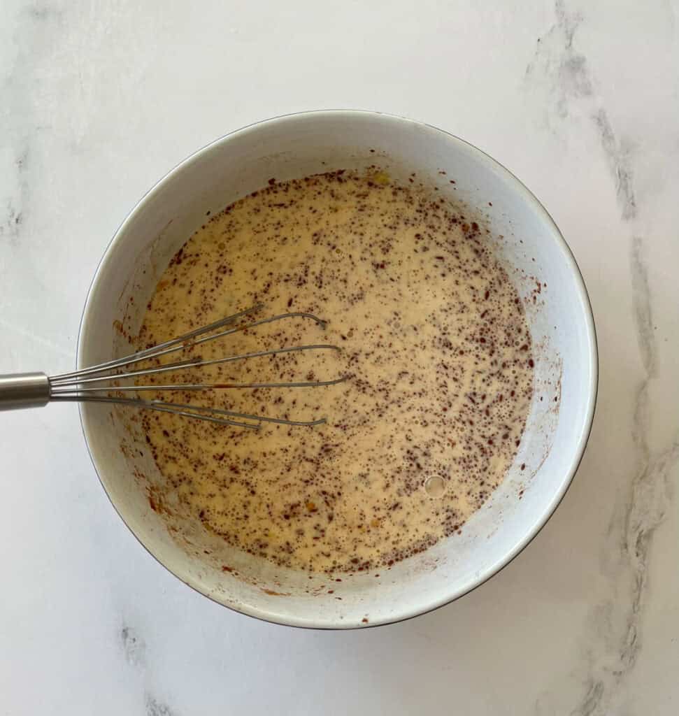 Egg, milk, and cinnamon mixture in a white bowl with a whisk.