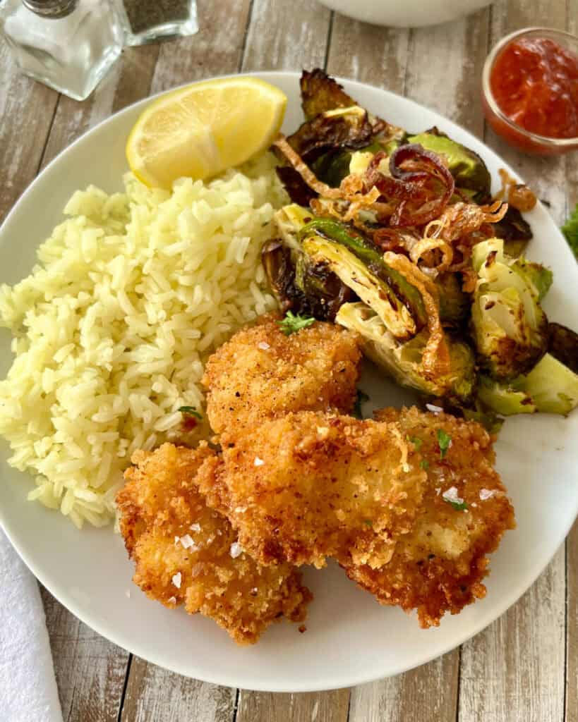 Crispy fried scallops served with rice, roasted Brussels sprouts, and lemon wedge.