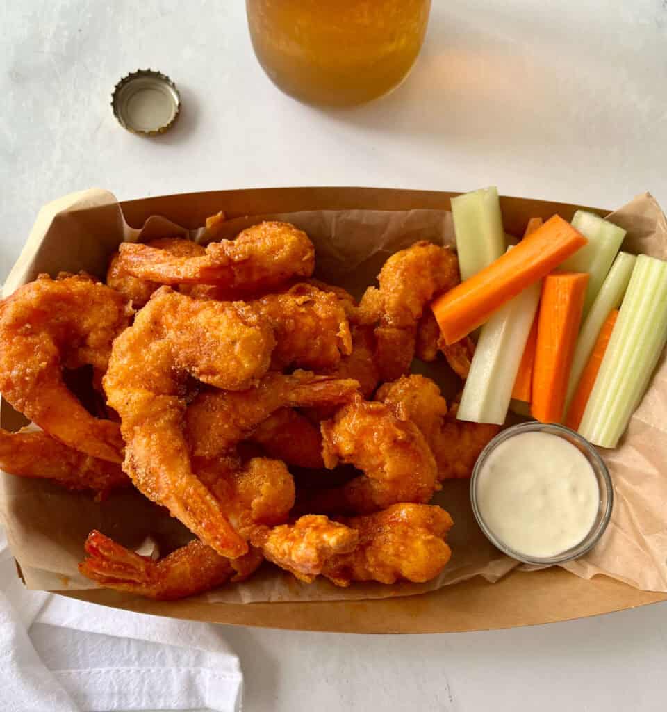 Fried shrimp accompanied by crunchy celery, carrots, and celery sticks with a side of dipping sauce for a tasty treat.