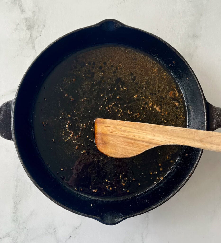 A cast iron pot with leftover broth and herbs, wooden spoon resting inside.