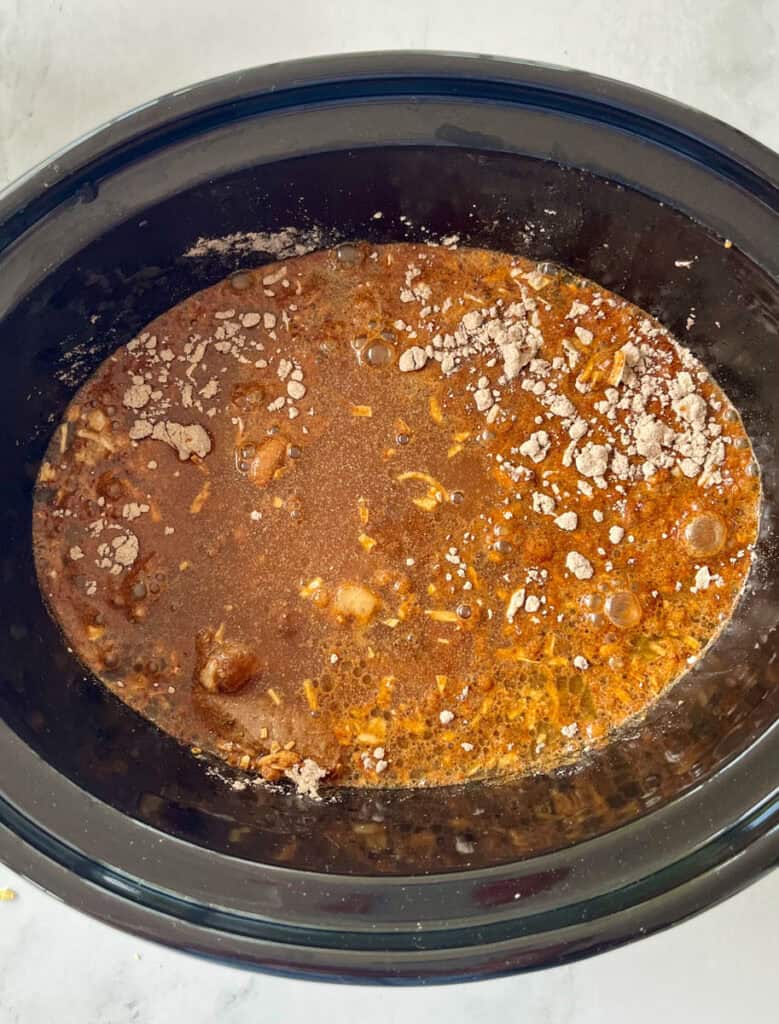Beef in juices and seasonings simmering in a black slow cooker on a marbled surface.