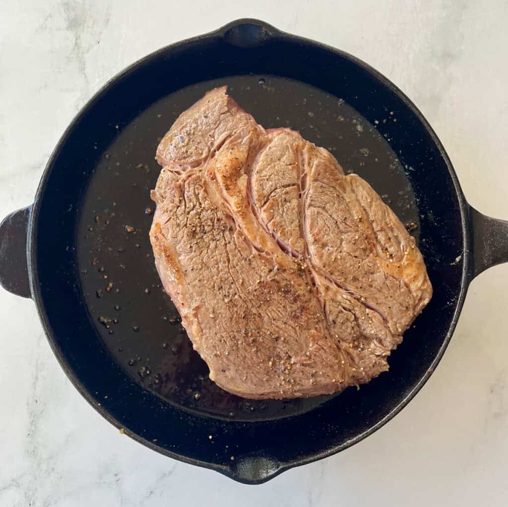 A close-up of a seasoned steak cooking in a cast iron skillet.