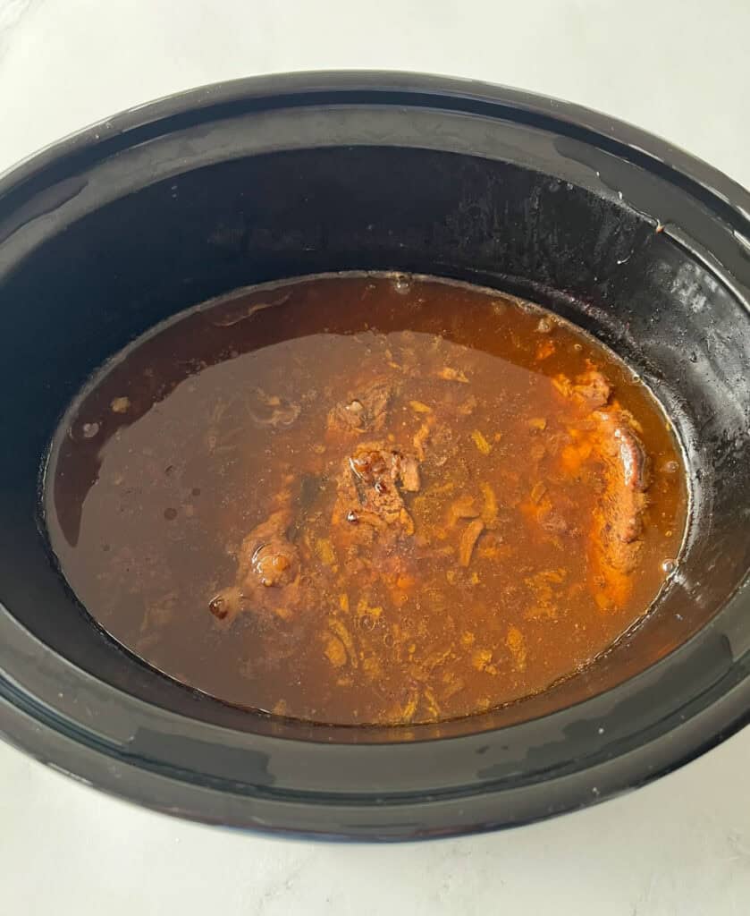 A close-up of a slow cooker filled with tender beef and broth.