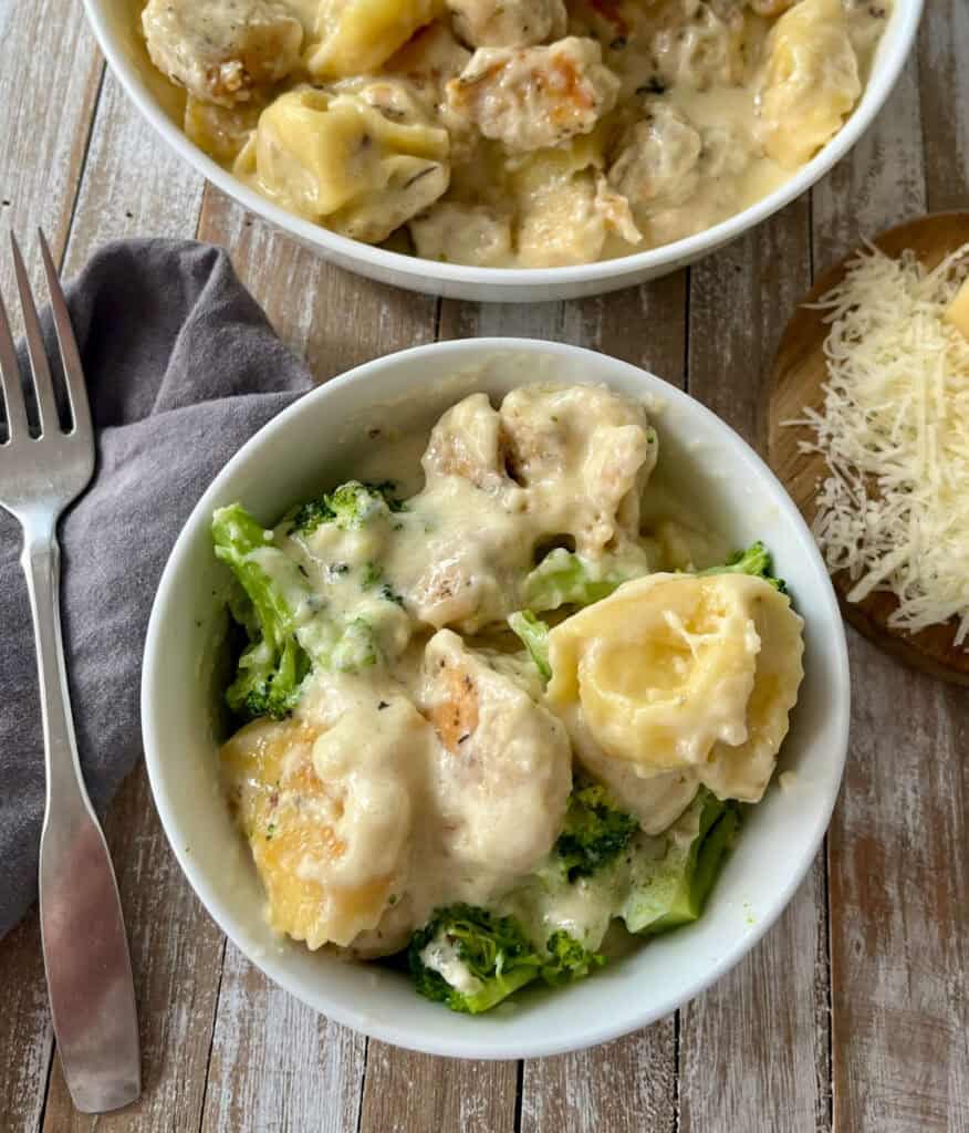 Creamy chicken tortellini in a cheese sauce with broccoli, served in a white bowl on a rustic wooden surface.