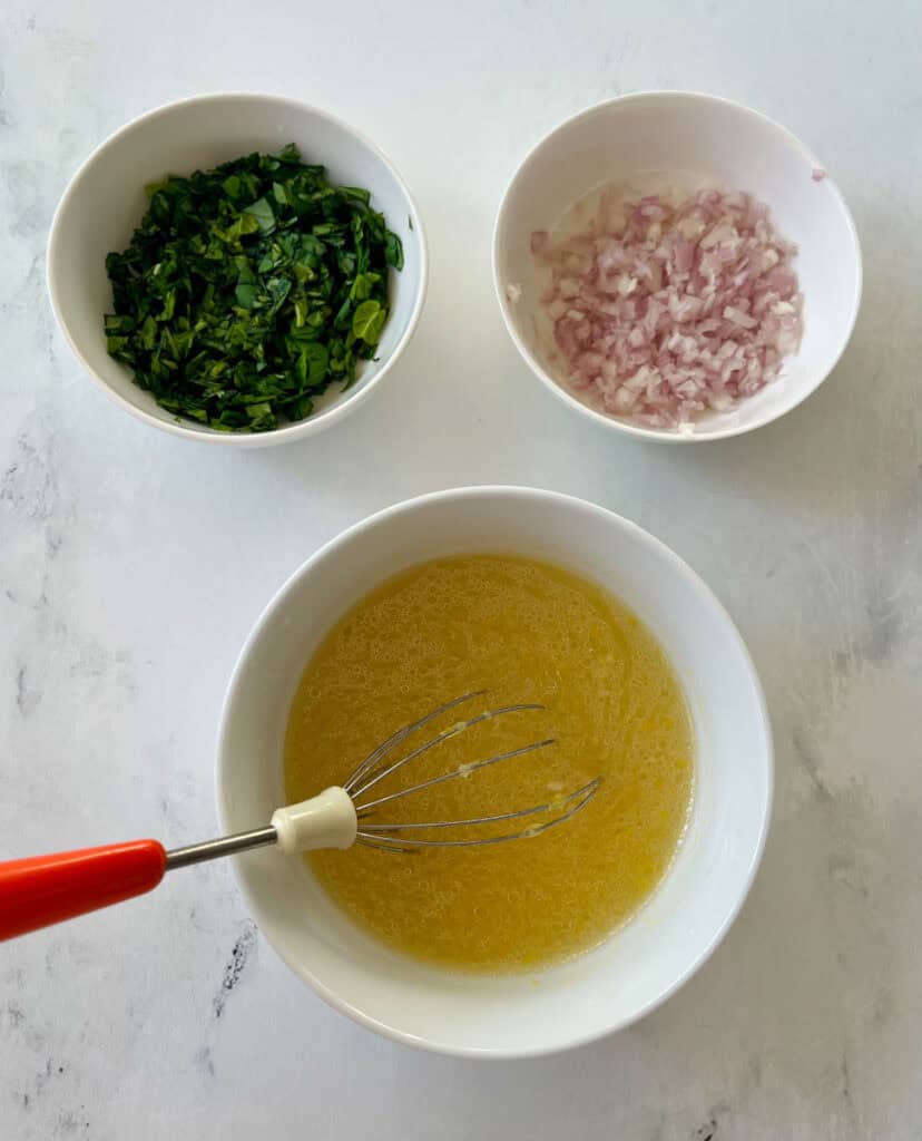 Bowls with chopped herbs, diced onions, vinegar, and oil on a marbled surface.