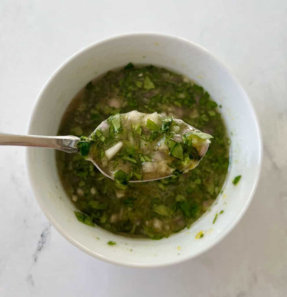 Close up of a basil lemon vinaigrette in a small white bowl on a marbled surface.