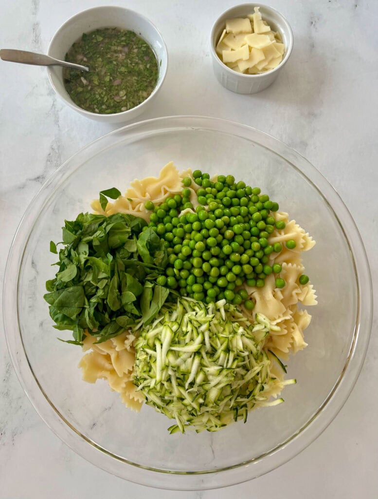 Fresh green peas, chopped zucchini, spinach, and pasta in a glass bowl.