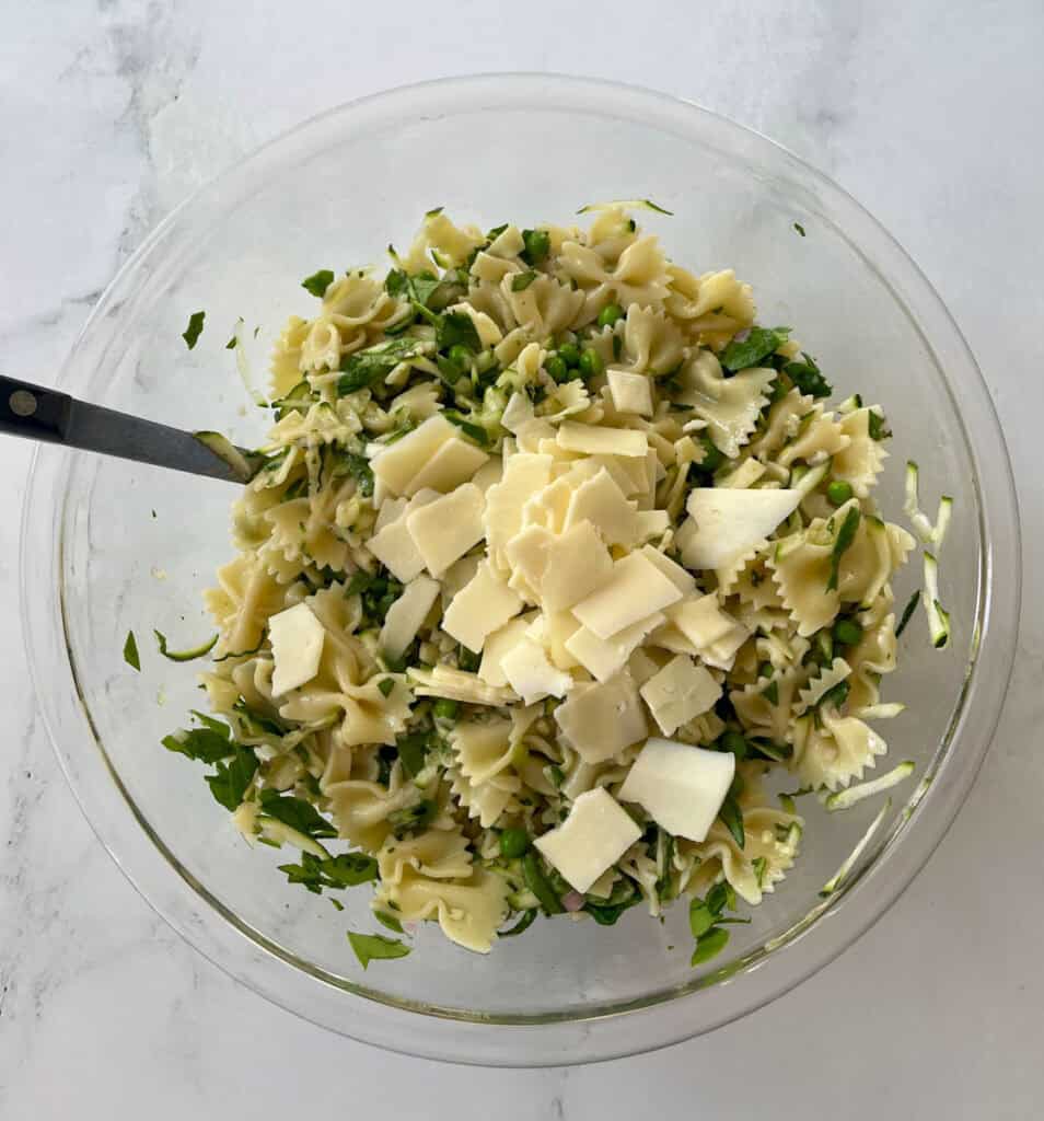 Fresh pasta salad with herbs and cheese in a glass bowl on a marbled surface.