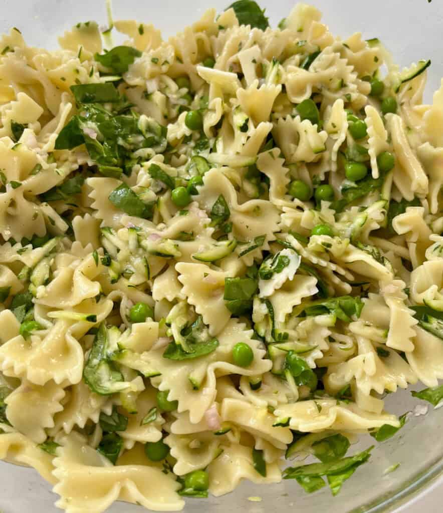 Pasta with zucchini, spinach, peas., basil in a vinaigrette dressing in a large glass bowl.