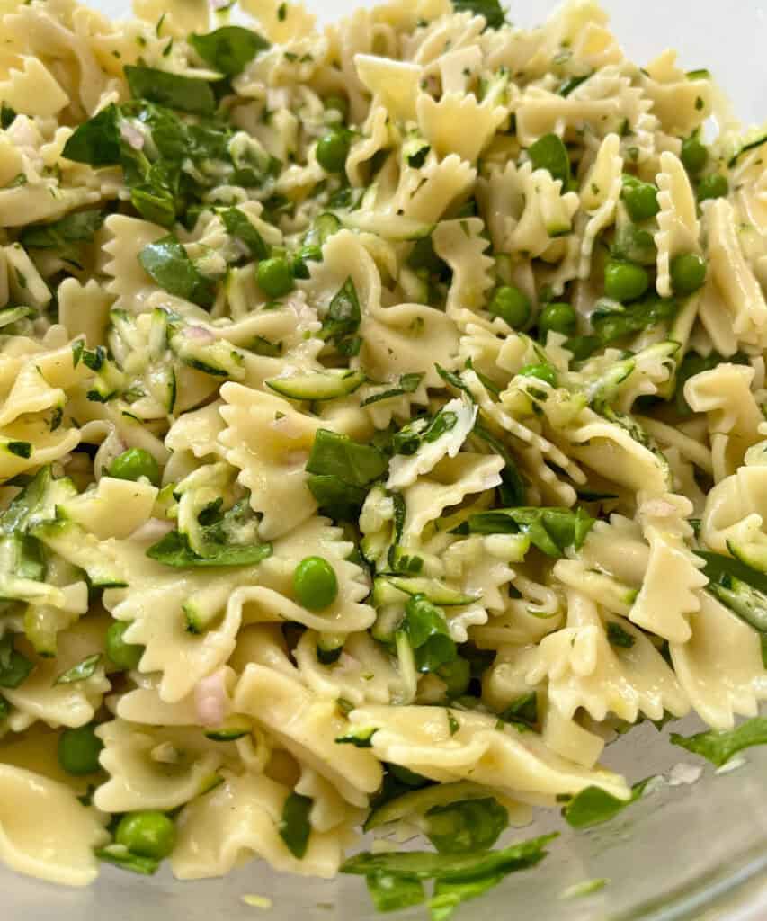 Close up of pasta salad with zucchini, spinach, peas, basil, and lemon basil vinaigrette, garnished with fresh basil.
