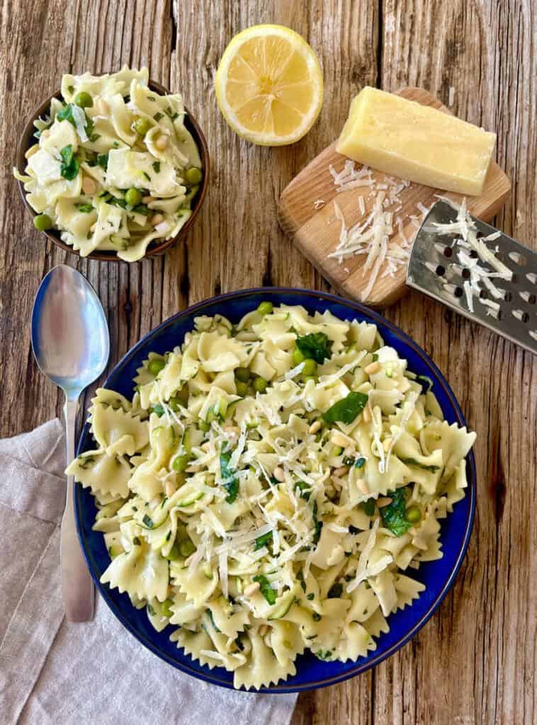 Cold pasta with shredded zucchini, spinach, peas, basil and cheese in a bowl on a rustic wood surface.