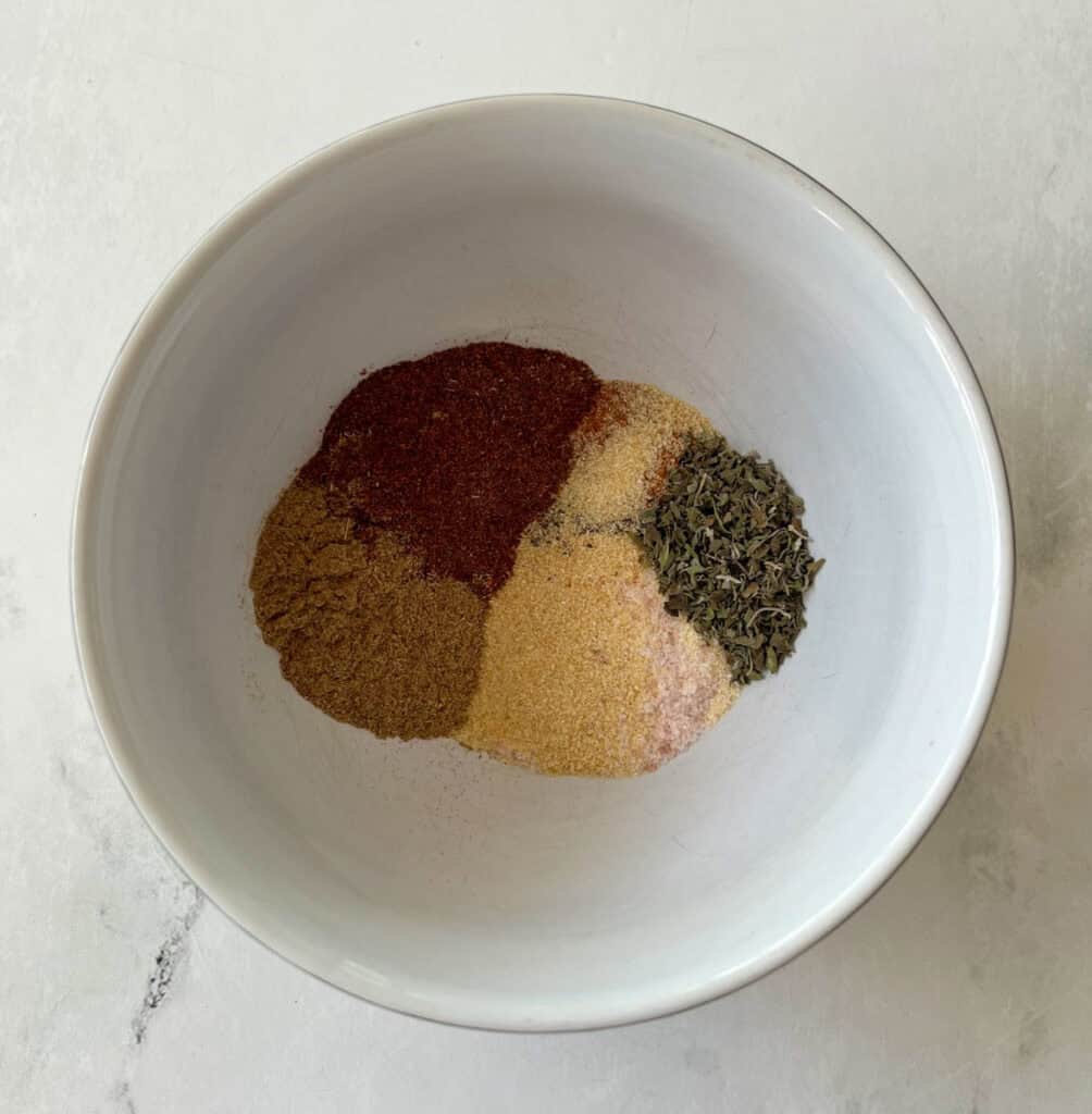 Spice blend with chili powder, cumin, thyme, salt, garlic powder, and pepper in a white bowl.