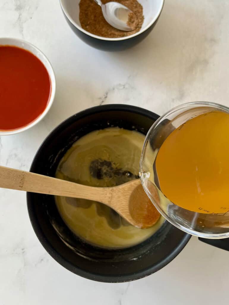 Sauce with broth, spices, and fresh ingredients in a black saucepan.