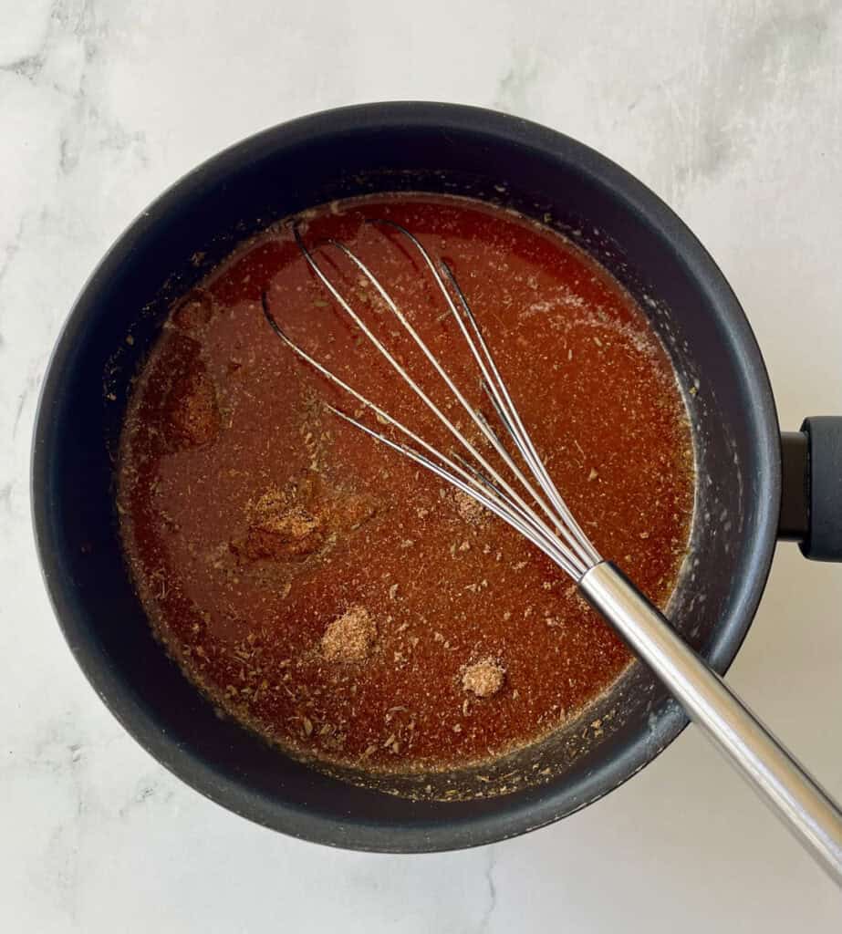 Sauce cooking in a black saucepan with a whisk for stirring.