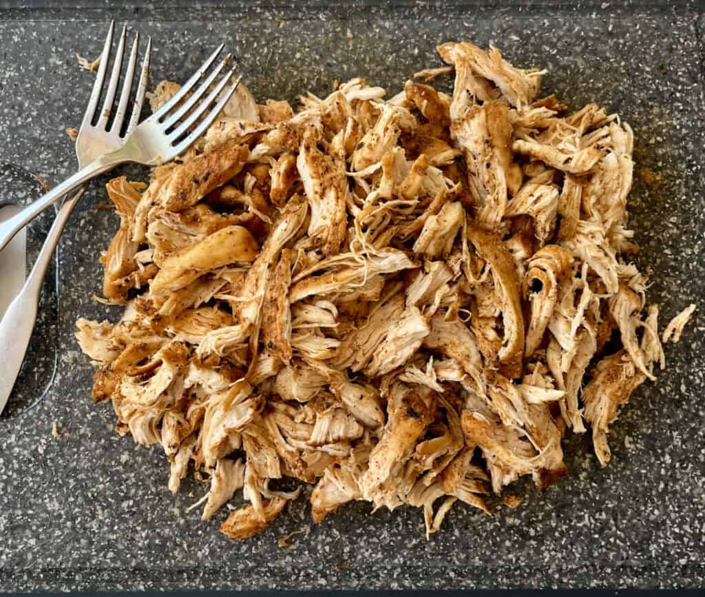 Shredded cooked chicken meat on a dark textured surface, ready for recipes or meal prep.