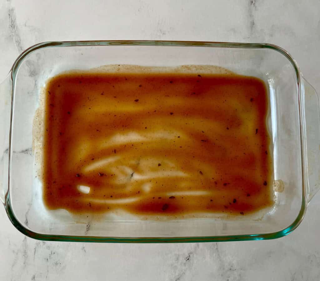 Homemade enchilada sauce in a clear glass baking dish on a marbled surface.