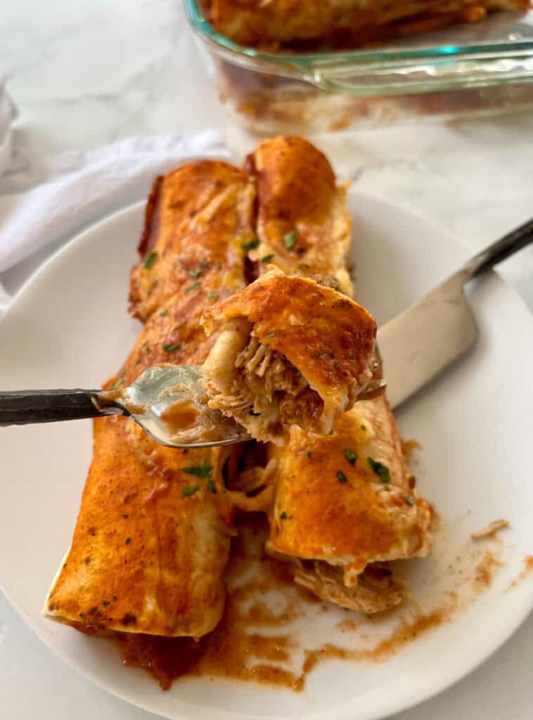 Close-up of golden-brown chicken enchiladas filled with seasoned chicken and cheese, topped with sauce and herbs.