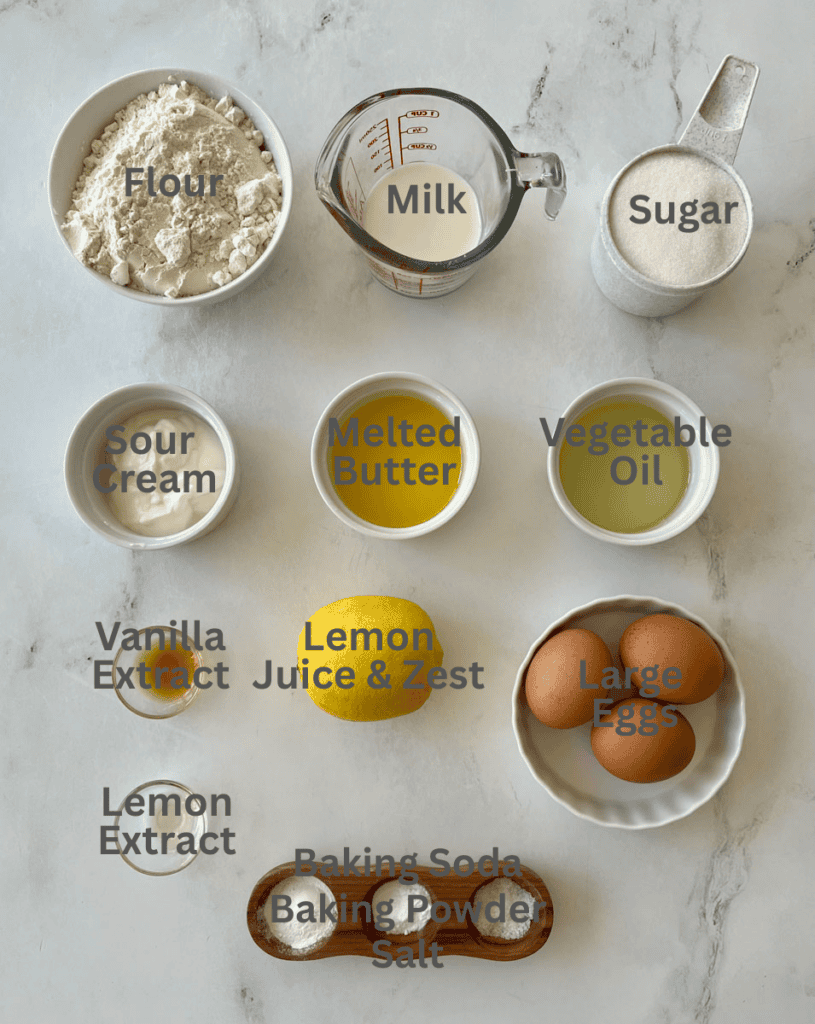Baking ingredients for lemon loaf, including flour, milk, sugar, sour cream, melted butter, vegetable oil, eggs, lemon extract, baking soda, baking powder, and salt.