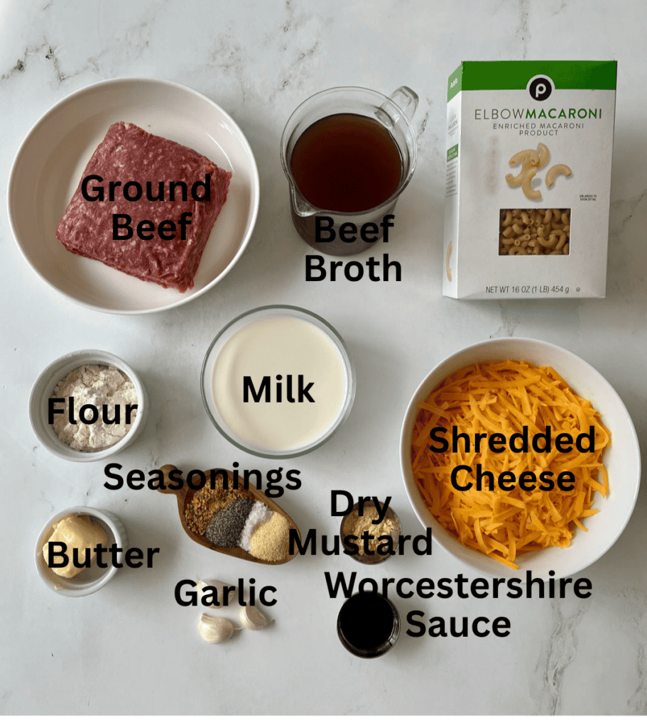 Ingredients for preparing homemade macaroni and cheese, including ground beef, shredded cheese, milk, and seasonings on a white surface.