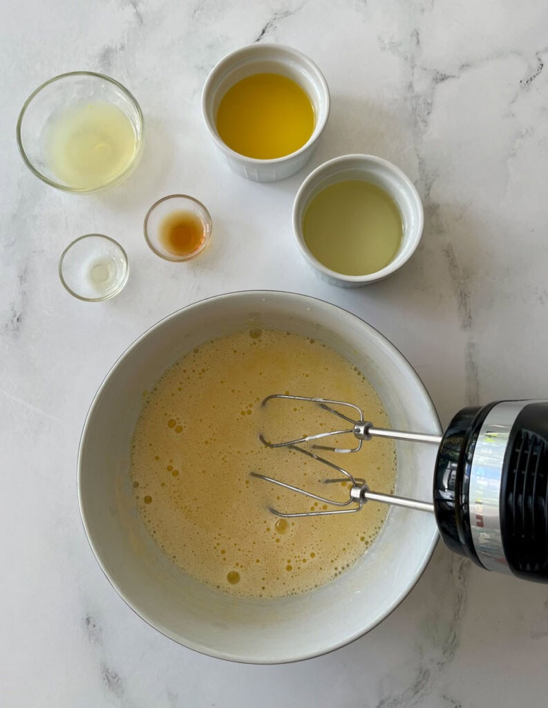 Egg mixture with oils and liquids in a bowl, with a hand mixer.